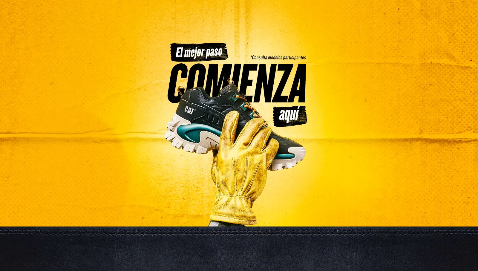 Bota industrial Caterpillar para hombre en negro y verde oliva. Sostenida por un guante de trabajo de cuero amarillo sobre fondo amarillo.