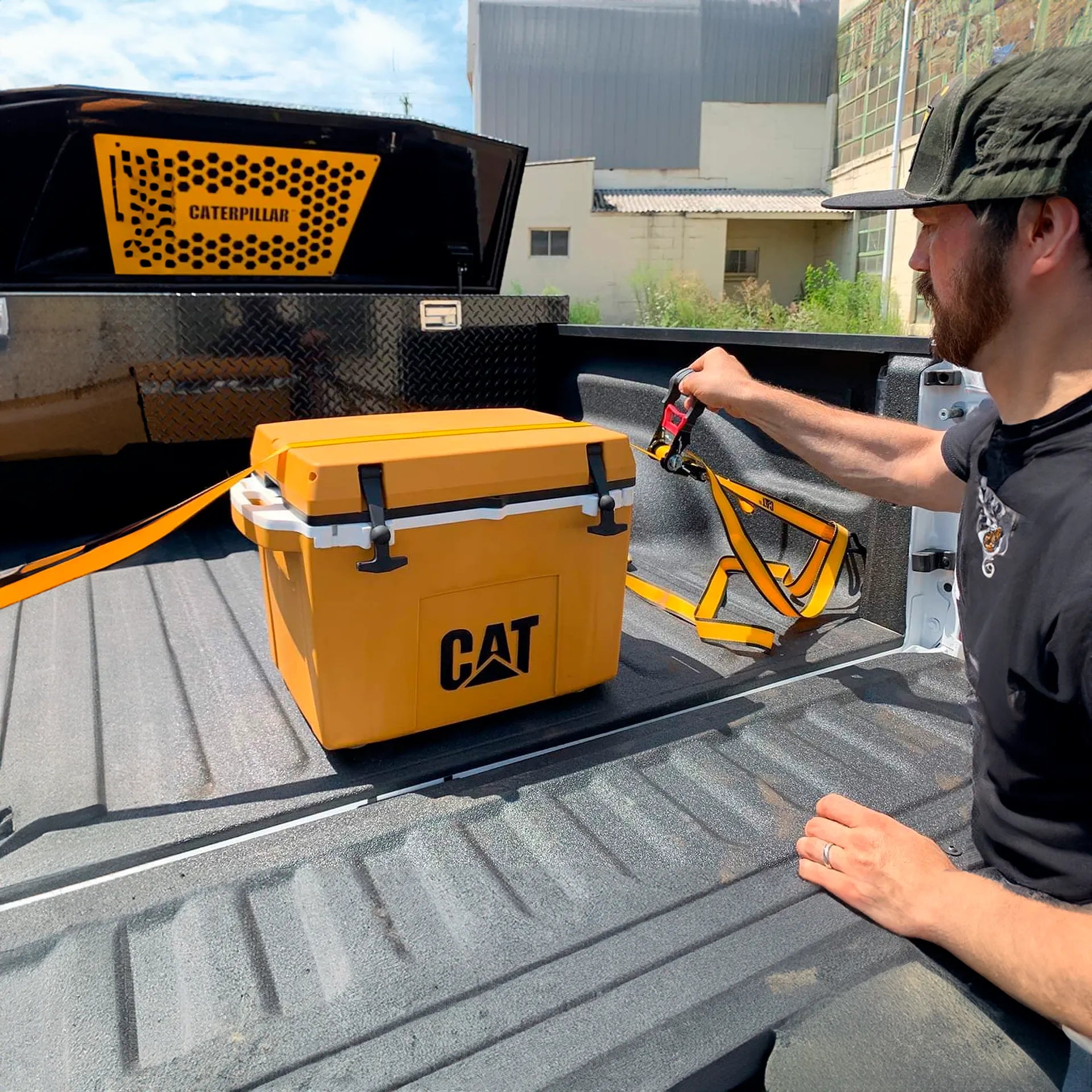 ombre asegurando una hielera amarilla marca Cat en la caja de una camioneta
